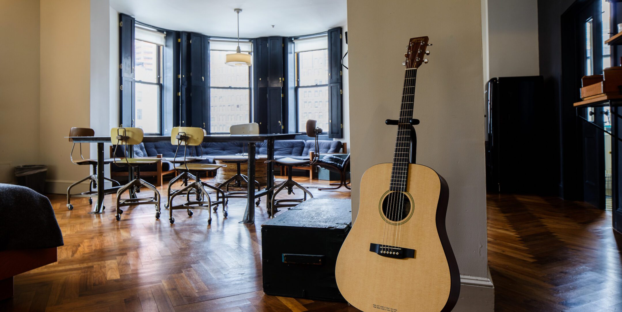 A nicely lit meeting space with plenty of seating and tables. As you enter the room, there is a guitar on display.
