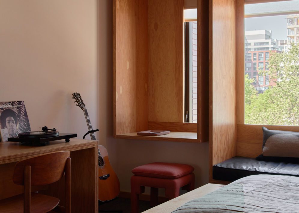 A record player and records sit against a window; a red footstool sits on the floor