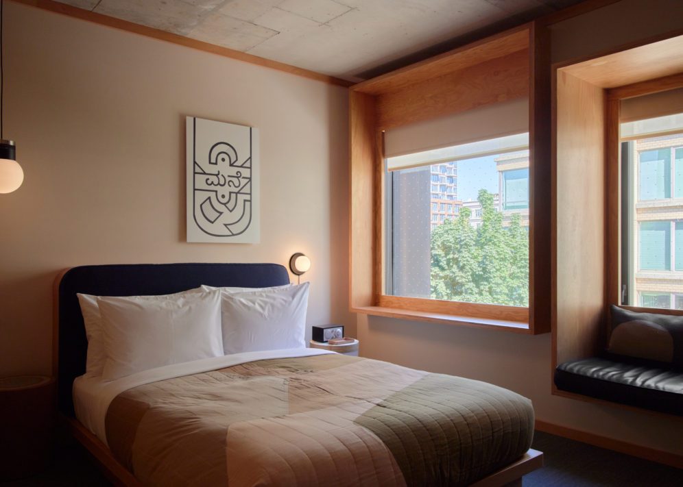 A bed sits next to a wall featuring two windows and a black leather seating area