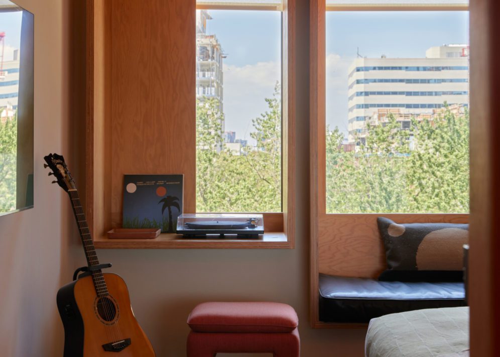 A record player and records sit against a window; a red footstool sits on the floor