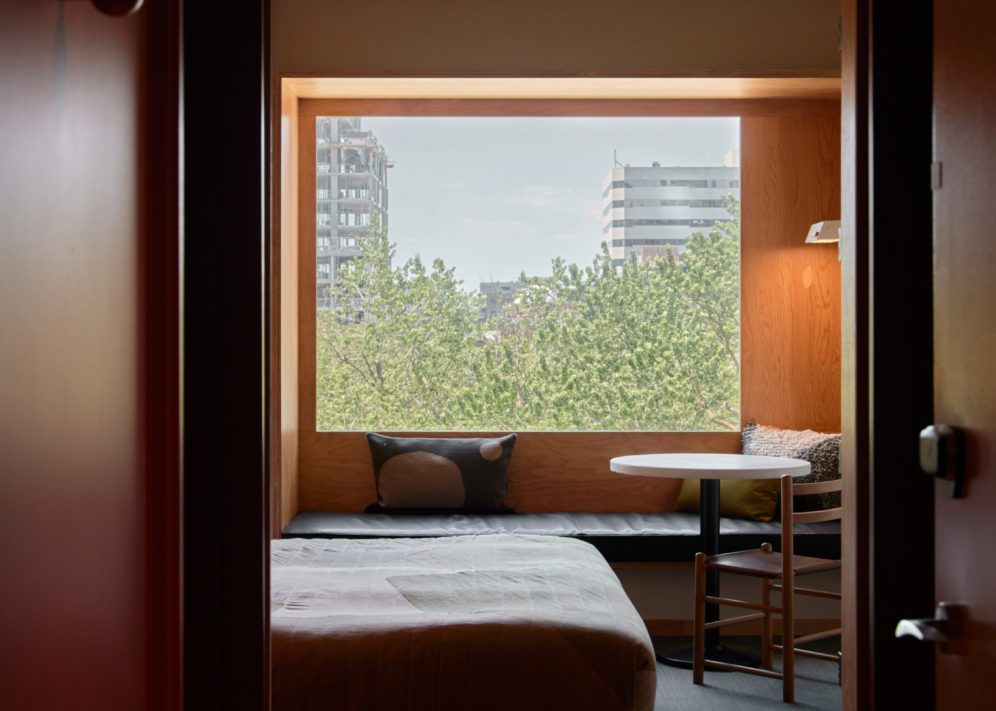 A wood paneled room features a black leather seating area under a window featuring greenery