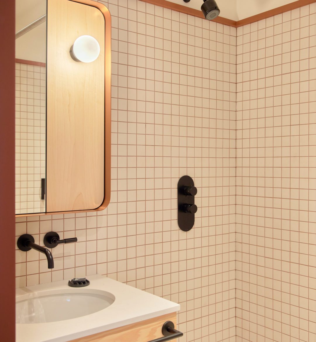 A modern white tiled bathroom features temperature knobs built into the wall