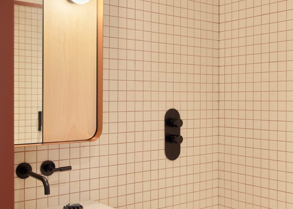 A modern white tiled bathroom features temperature knobs built into the wall