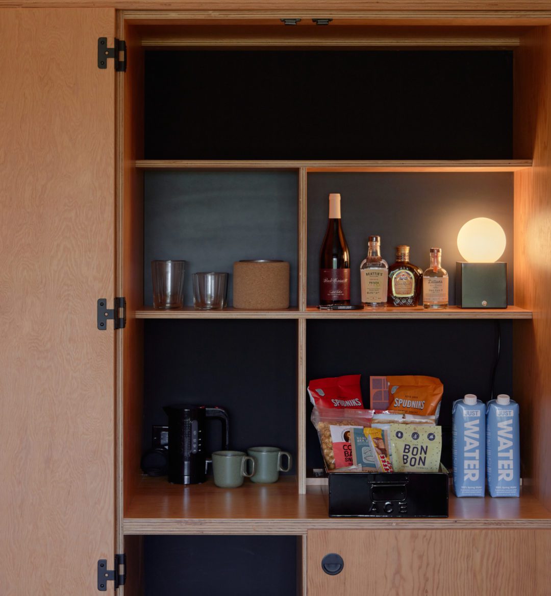A minibar features alcohol, water and other snacks; next to it is a coffee maker and mugs