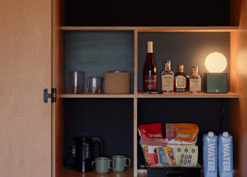 A minibar features alcohol, water and other snacks; next to it is a coffee maker and mugs