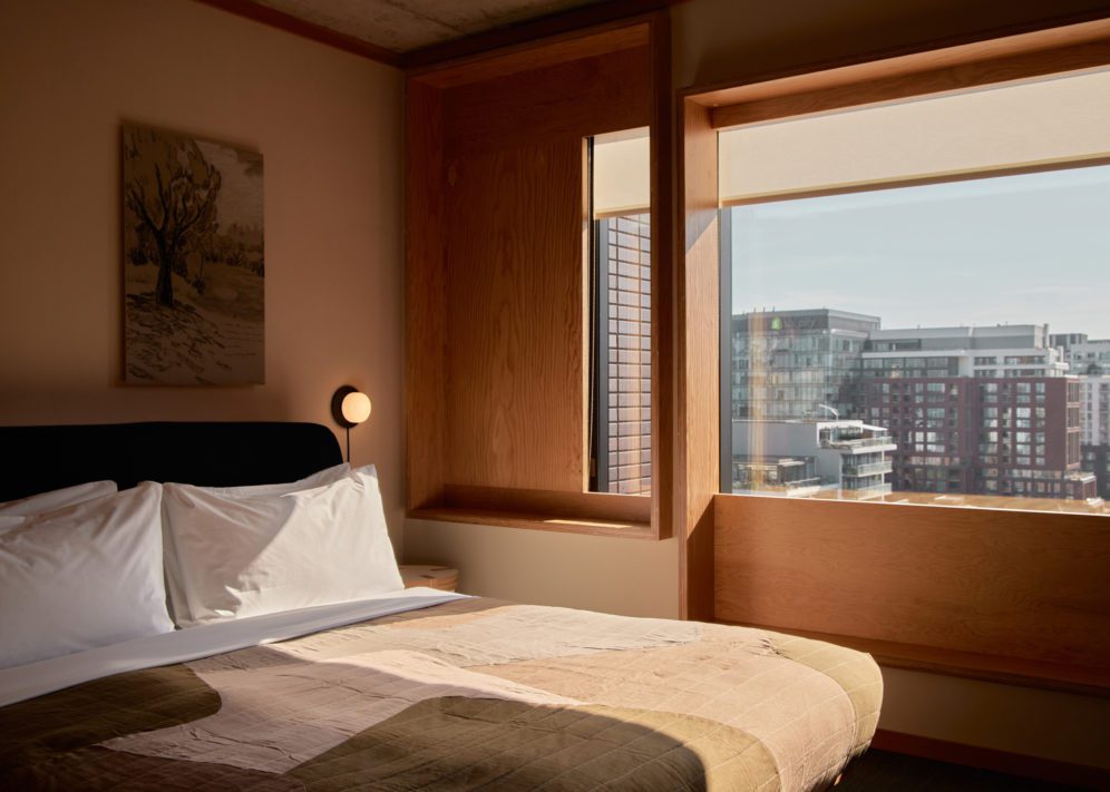 A bed sits next to two windows, offering expansive views of the city