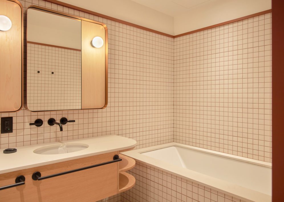 A modern white tiled bathroom features a deep bathtub