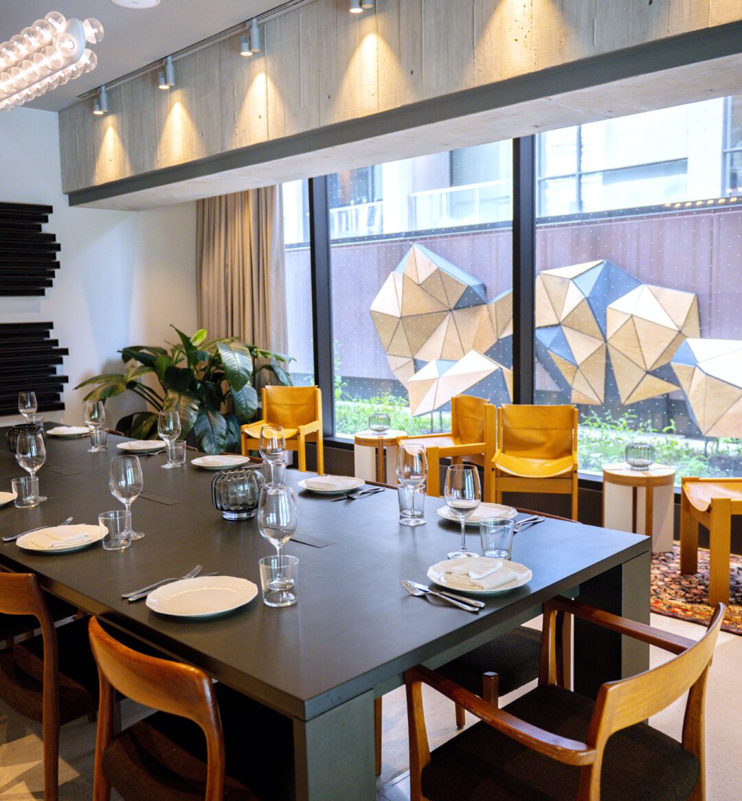 Modern dining room with a long black table, wooden chairs, large windows, and geometric wall art outside.