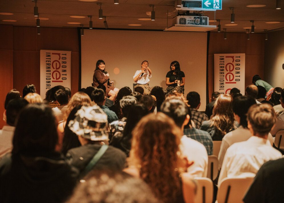 Three panelists speak on stage to an audience at a Toronto Reel Asian International Film Festival event in a conference room.
